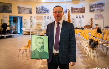 W&oacute;jt Grzegorz Wegrzynowski pozuje do zdjęcia z portretem Ignacego Łukasiewicza, kt&oacute;ry został wykonany oł&oacute;wkiem przez lokalna artystkę Magdalenę Pacek.  