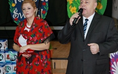 Kobieta w stroju ludowym oraz mężczyzna w ciemnym garniturze witają gości. 