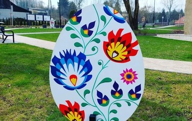 Metrowa pisanka wykonana z drewna. Na niej niebieskie oraz czerwono ż&oacute;łte kwiaty.kwiaty. Pisanka umieszczona na skwerku w Chork&oacute;wce. 