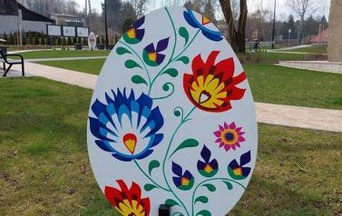 Metrowa pisanka wykonana z drewna. Na niej niebieskie oraz czerwono ż&oacute;łte kwiaty.kwiaty. Pisanka umieszczona na skwerku w Chork&oacute;wce. 