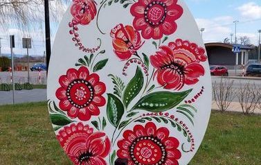 Metrowa pisanka wykonana z drewna. Na niej r&oacute;żowe kwiaty. Pisanka umieszczona na skwerku w Chork&oacute;wce. 