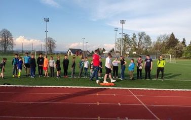 Na murawie Kompleksu Boisk Sportowych stoją organizatorzy oraz uczestnicy maj&oacute;wki. 
