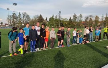 Na murawie Kompleksu Boisk Sportowych stoją organizatorzy oraz uczestnicy maj&oacute;wki. 
