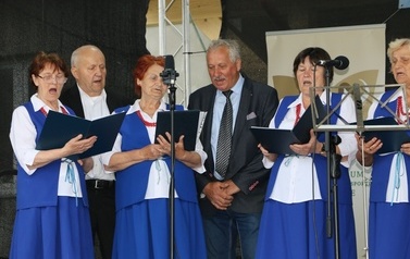 Zesp&oacute;ł śpiewaczy w niebieskich strojach. Kobiety i mężczyźni. 