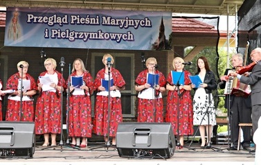 Zesp&oacute;ł śpiewaczy w czerwonych strojach. Kobiety i mężczyźni. 