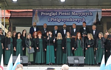 Ch&oacute;r mieszany legato. Kobiety w ciemnozielonych sukniach oraz elegancko ubrani mężczyźni. 