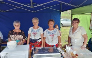 Panie z KGW, na stroiku kulinarnym. Kobiety ubrane w białe bluzki i kwieciste sp&oacute;dnice. 