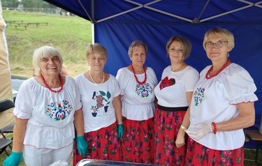 Panie z KGW, na stroiku kulinarnym. Kobiety ubrane w białe bluzki i kwieciste sp&oacute;dnice. 