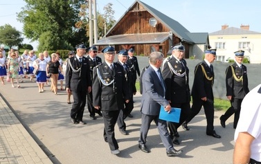 Przemarsz uczestnik&oacute;w spotkania. Jako pierwsze idą mażoretki, następnie orkiestra dęta, zaproszeni goście i gospodarze uroczystości. 