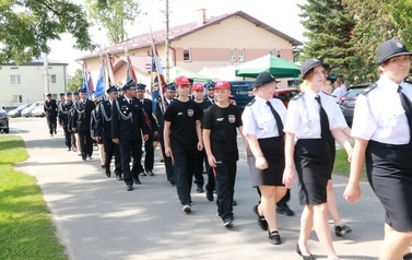 Przemarsz uczestnik&oacute;w spotkania. Jako pierwsze idą mażoretki, następnie orkiestra dęta, zaproszeni goście i gospodarze uroczystości. 