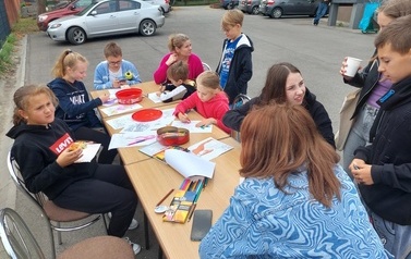 Zdjęcie dzieci i młodzieży, kt&oacute;ra przy przygotowanych dla nich stolikach koloruje malowanki tematyczne. 