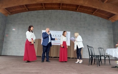 Narodowe czytanie w Gminie Chork&oacute;wka. Stacjonarna scena a na niej szyld Narodowego czytania, na białym tle czarne litery i napis Narodowe czytanie, wplecione elementy czerwone. Na scenie okrągły stolik na nim czerwony bukiet. Przy stoliku krzesła na kt&oacute;ry