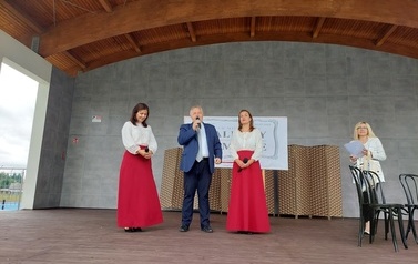 Narodowe czytanie w Gminie Chork&oacute;wka. Stacjonarna scena a na niej szyld Narodowego czytania, na białym tle czarne litery i napis Narodowe czytanie, wplecione elementy czerwone. Na scenie okrągły stolik na nim czerwony bukiet. Przy stoliku krzesła na kt&oacute;ry
