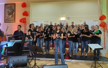 	 Zdjęcie ch&oacute;ru mieszanego Legato. Ch&oacute;r w luźnych strojach dzinsach i koszulkach z nazwa ch&oacute;ry. w tych stylizacjach wykonywali swoje interpretacje piosenek wsp&oacute;łczesnych. Na przodzie solista ch&oacute;ru oraz dyrygentka. 