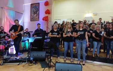 	 Zdjęcie ch&oacute;ru mieszanego Legato. Ch&oacute;r w luźnych strojach dzinsach i koszulkach z nazwa ch&oacute;ry. w tych stylizacjach wykonywali swoje interpretacje piosenek wsp&oacute;łczesnych. Na przodzie trzy solistki ch&oacute;ru oraz dyrygentka. 