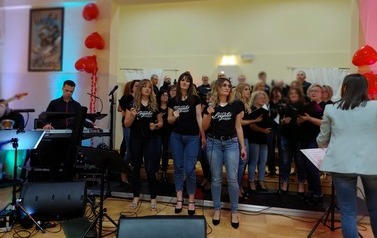 	 Zdjęcie ch&oacute;ru mieszanego Legato. Ch&oacute;r w luźnych strojach dzinsach i koszulkach z nazwa ch&oacute;ry. w tych stylizacjach wykonywali swoje interpretacje piosenek wsp&oacute;łczesnych. Na przodzie solista ch&oacute;ru oraz dyrygentka. 