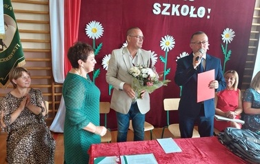 Na zdjęciu Helena Nowak oraz grono pedagogiczne. Są r&oacute;wnież W&oacute;jt i Zastępca kt&oacute;rzy wręczają kwiaty oraz dyplom. 