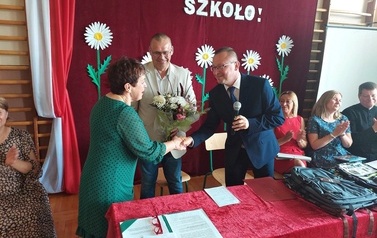 Na zdjęciu Helena Nowak oraz grono pedagogiczne. Są r&oacute;wnież W&oacute;jt i Zastępca kt&oacute;rzy wręczają kwiaty oraz dyplom. 