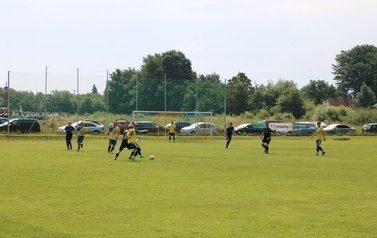 Zdjęcie wykonane podczas meczu. Zawodnicy na boisku sportowym braja w piłkę nożną. 