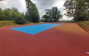 Widoczne w oddali boisko sportowe w kolorze niebiesko-pomarańczowym.