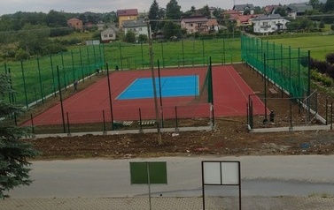 Widoczne w oddali boisko sportowe w kolorze niebiesko-pomarańczowym.