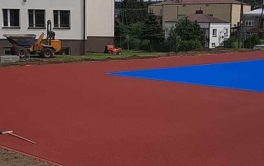 Widoczne w oddali boisko sportowe w kolorze niebiesko-pomarańczowym.