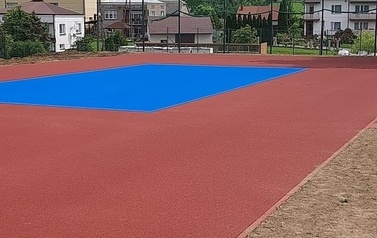 Widoczne w oddali boisko sportowe w kolorze niebiesko-pomarańczowym.