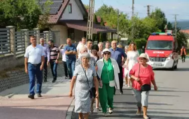 Poch&oacute;d dożynkowy. Korow&oacute;d wielu os&oacute;b ubranych elegancko, a także w stroje ludowe. Kobiety niosą dożynkowe wieńce. Niosą także chleby