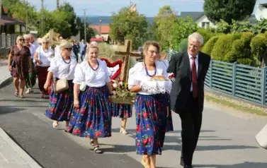 Poch&oacute;d dożynkowy. Korow&oacute;d wielu os&oacute;b ubranych elegancko, a także w stroje ludowe. Kobiety niosą dożynkowe wieńce. Niosą także chleby