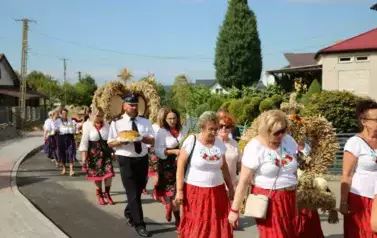 Poch&oacute;d dożynkowy. Korow&oacute;d wielu os&oacute;b ubranych elegancko, a także w stroje ludowe. Kobiety niosą dożynkowe wieńce. Niosą także chleby