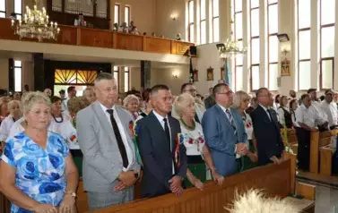 Poch&oacute;d dożynkowy. Korow&oacute;d wielu os&oacute;b ubranych elegancko, a także w stroje ludowe. Kobiety niosą dożynkowe wieńce. Niosą także chleby