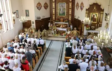 Poch&oacute;d dożynkowy. Korow&oacute;d wielu os&oacute;b ubranych elegancko, a także w stroje ludowe. Kobiety niosą dożynkowe wieńce. Niosą także chleby