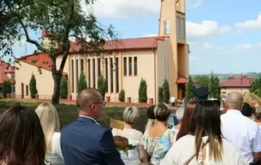 Poch&oacute;d dożynkowy. Korow&oacute;d wielu os&oacute;b ubranych elegancko, a także w stroje ludowe. Kobiety niosą dożynkowe wieńce. Niosą także chleby