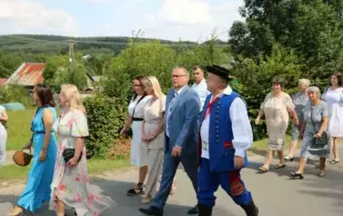 Poch&oacute;d dożynkowy. Korow&oacute;d wielu os&oacute;b ubranych elegancko, a także w stroje ludowe. Kobiety niosą dożynkowe wieńce. Niosą także chleby