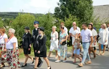 Poch&oacute;d dożynkowy. Korow&oacute;d wielu os&oacute;b ubranych elegancko, a także w stroje ludowe. Kobiety niosą dożynkowe wieńce. Niosą także chleby