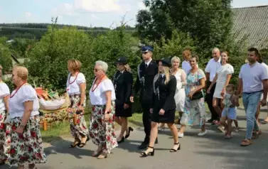 Poch&oacute;d dożynkowy. Korow&oacute;d wielu os&oacute;b ubranych elegancko, a także w stroje ludowe. Kobiety niosą dożynkowe wieńce. Niosą także chleby