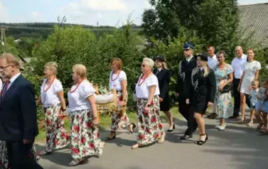 Poch&oacute;d dożynkowy. Korow&oacute;d wielu os&oacute;b ubranych elegancko, a także w stroje ludowe. Kobiety niosą dożynkowe wieńce. Niosą także chleby
