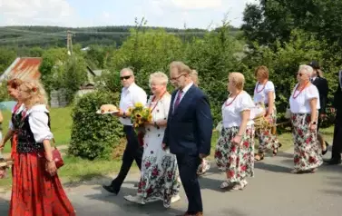 Poch&oacute;d dożynkowy. Korow&oacute;d wielu os&oacute;b ubranych elegancko, a także w stroje ludowe. Kobiety niosą dożynkowe wieńce. Niosą także chleby