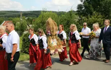Poch&oacute;d dożynkowy. Korow&oacute;d wielu os&oacute;b ubranych elegancko, a także w stroje ludowe. Kobiety niosą dożynkowe wieńce. Niosą także chleby