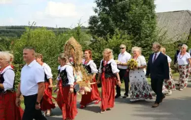 Poch&oacute;d dożynkowy. Korow&oacute;d wielu os&oacute;b ubranych elegancko, a także w stroje ludowe. Kobiety niosą dożynkowe wieńce. Niosą także chleby