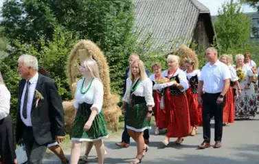 Poch&oacute;d dożynkowy. Korow&oacute;d wielu os&oacute;b ubranych elegancko, a także w stroje ludowe. Kobiety niosą dożynkowe wieńce. Niosą także chleby