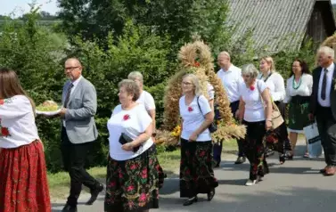 Poch&oacute;d dożynkowy. Korow&oacute;d wielu os&oacute;b ubranych elegancko, a także w stroje ludowe. Kobiety niosą dożynkowe wieńce. Niosą także chleby