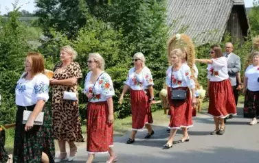 Poch&oacute;d dożynkowy. Korow&oacute;d wielu os&oacute;b ubranych elegancko, a także w stroje ludowe. Kobiety niosą dożynkowe wieńce. Niosą także chleby
