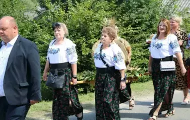 Poch&oacute;d dożynkowy. Korow&oacute;d wielu os&oacute;b ubranych elegancko, a także w stroje ludowe. Kobiety niosą dożynkowe wieńce. Niosą także chleby