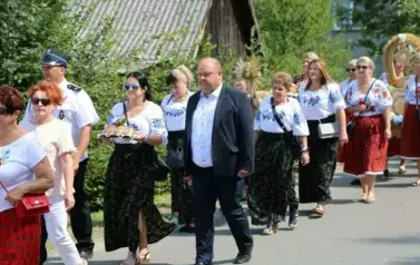 Poch&oacute;d dożynkowy. Korow&oacute;d wielu os&oacute;b ubranych elegancko, a także w stroje ludowe. Kobiety niosą dożynkowe wieńce. Niosą także chleby