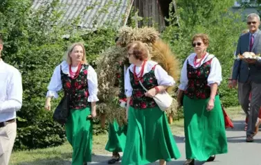 Poch&oacute;d dożynkowy. Korow&oacute;d wielu os&oacute;b ubranych elegancko, a także w stroje ludowe. Kobiety niosą dożynkowe wieńce. Niosą także chleby