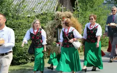 Poch&oacute;d dożynkowy. Korow&oacute;d wielu os&oacute;b ubranych elegancko, a także w stroje ludowe. Kobiety niosą dożynkowe wieńce. Niosą także chleby