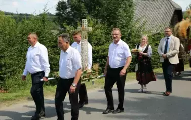 Poch&oacute;d dożynkowy. Korow&oacute;d wielu os&oacute;b ubranych elegancko, a także w stroje ludowe. Kobiety niosą dożynkowe wieńce. Niosą także chleby