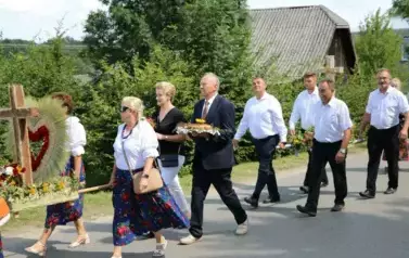 Poch&oacute;d dożynkowy. Korow&oacute;d wielu os&oacute;b ubranych elegancko, a także w stroje ludowe. Kobiety niosą dożynkowe wieńce. Niosą także chleby