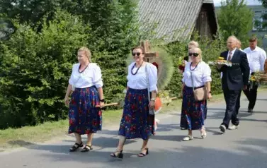 Poch&oacute;d dożynkowy. Korow&oacute;d wielu os&oacute;b ubranych elegancko, a także w stroje ludowe. Kobiety niosą dożynkowe wieńce. Niosą także chleby